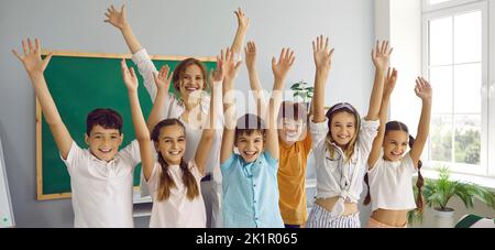 Lustige Gruppe von Klassenkameraden der Grundschule und ihre Lehrerin, die Spaß im Klassenzimmer haben. Stockfoto