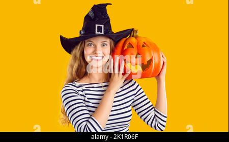 Porträt einer glücklichen schönen jungen Frau in einem Hexenhut mit einem Halloween Kürbis Stockfoto