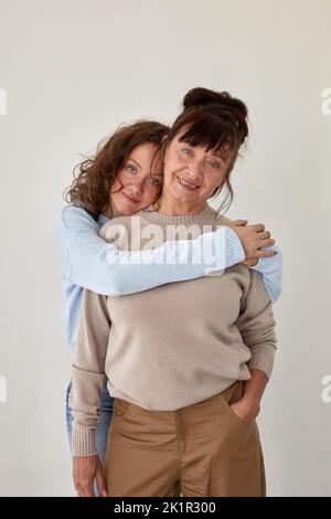 Junge Frau umarmt reife lächelnde Dame in lässiger Kleidung Stockfoto