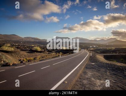 Die Straße LZ-30 durch die Weinberge der La Geria Landschaft auf der Insel Lanzarote, Spanien. Im Hintergrund vulkanische Berge des Timanfay Stockfoto