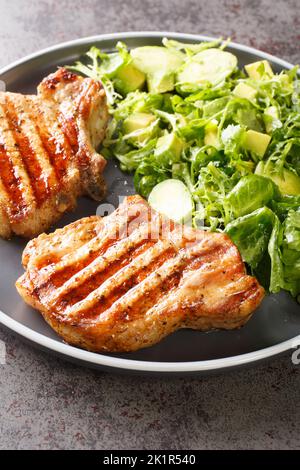 Gegrilltes Schweinesteak und grüner Gemüsesalat aus der Nähe auf dem Teller auf dem Tisch. Vertikal Stockfoto
