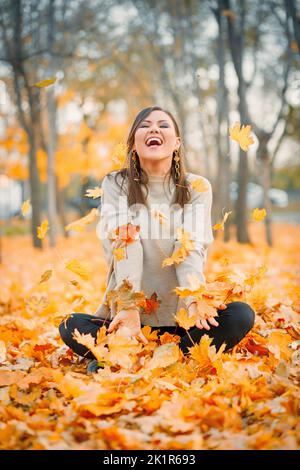 Lachende junge Frau, die im Herbstpark mit gefallenen Blättern spielt hat Stockfoto