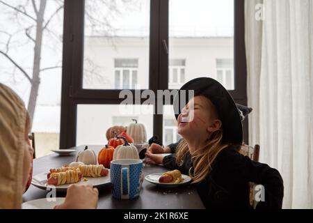 Lustiges Mädchen im Halloween Kostüm beim Essen am Tisch Stockfoto