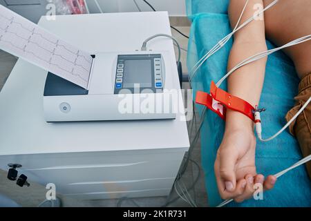 Herzelektrokardiographie für Kinder. EKG-Schreiber mit EKG-Ausdruck für Kinder, die im medizinischen Bett mit Vakuumsensoren liegen Stockfoto
