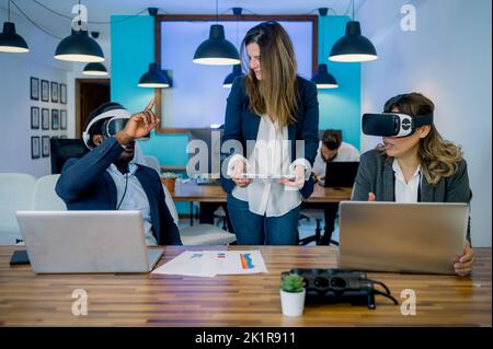 Multirassische Mitarbeiter, die im Büro Tablet-Laptops und VR-Brillen verwenden Stockfoto