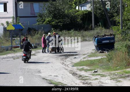 IZIUM, UKRAINE - 19. SEPTEMBER 2022 - die Menschen stehen in einer Straße in der Nähe eines umgedrehten Autos in Izium, befreit von russischen Eindringlingen, Region Charkiw, Norden Stockfoto