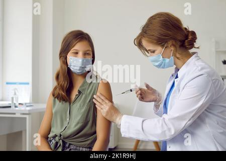 Glückliches Kind in medizinischer Gesichtsmaske, das gegen Grippe, Covid oder Monkeypox-Infektion geimpft wird Stockfoto