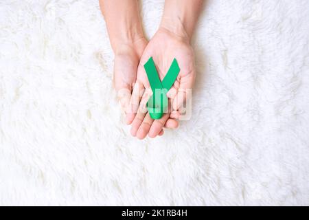 Grünes Band mit Handgriff zur Unterstützung von Menschen, die leben und krank sind. Konzept des Monats für Leber, Gallenbladen, Nierenkrebs und Lymphom-Bewusstsein Stockfoto