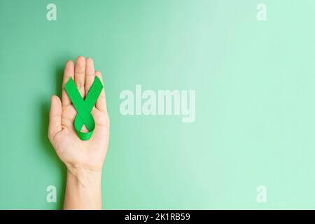 Grünes Band mit Handgriff zur Unterstützung von Menschen, die leben und krank sind. Konzept des Monats für Leber, Gallenbladen, Nierenkrebs und Lymphom-Bewusstsein Stockfoto