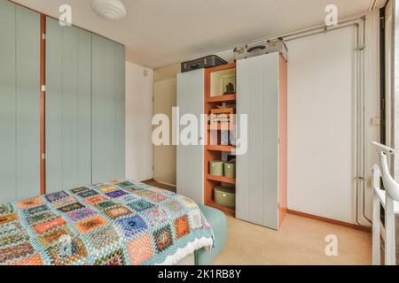 Komfortables Bett mit gepunkteter Federdecke in der Nähe von Kleiderschrank und Tisch mit Stuhl im minimalistischen Stil im modernen Apartment Stockfoto