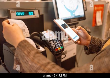 Seitenansicht der jungen Frau, die am Self-Checkout mit der Smartphone-App im Geschäft bezahlt Stockfoto