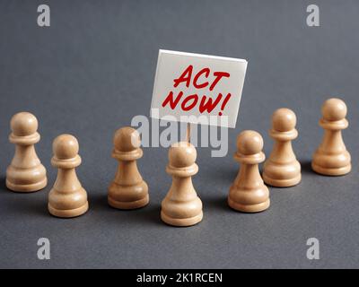 Schachfiguren-Protestler mit einem Schilderbanner mit der Botschaft HANDELN JETZT von der Menge umgeben. Jetzt handeln Konzept. Stockfoto