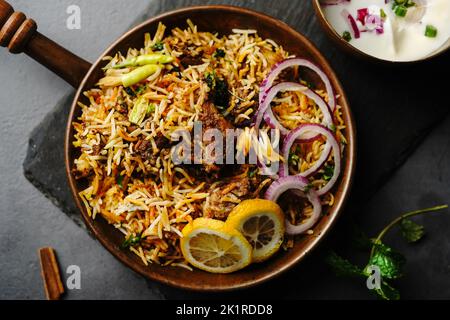 Hyderabadi Mutton Goat Biryani serviert mit Joghurt Raita in stimmungsvoller Umgebung Stockfoto