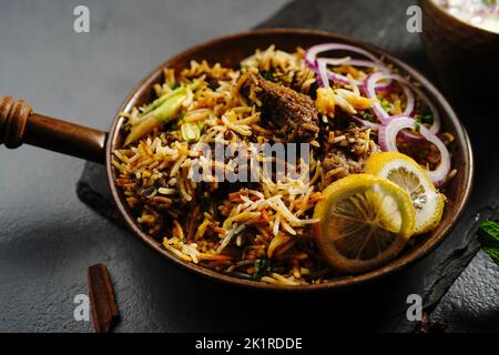 Hyderabadi Mutton Goat Biryani serviert mit Joghurt Raita in stimmungsvoller Umgebung Stockfoto