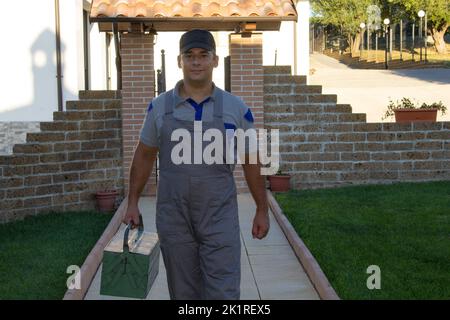 Bild eines lächelnden Handwerker Klempner mit Arbeitsüberalls und Werkzeugkasten. Rufen Sie einen Hausreparatur- und Do-it-yourself-Experten an Stockfoto