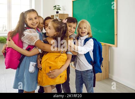 Glückliche kleine Grundschüler umarmen sich nach dem Treffen im Klassenzimmer. Stockfoto