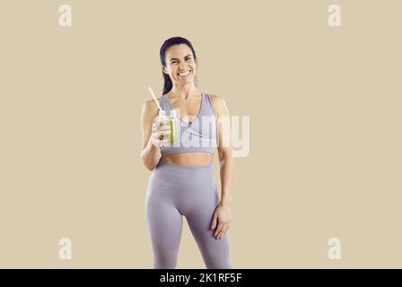 Fröhliche sportliche Frau mit einem Glas leckeren grünen Smoothie, isoliert auf beigem Hintergrund. Stockfoto