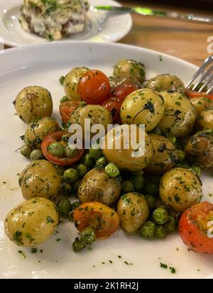 Junge kleine Kartoffeln mit Gemüse, Erbsen und Tomaten auf einem Teller. Stockfoto