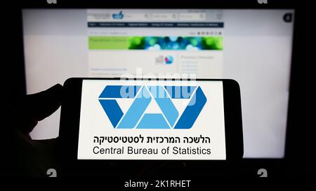 Person mit Mobiltelefon und Logo des israelischen Zentralbüros für Statistik (CBS) auf dem Bildschirm vor der Webseite. Konzentrieren Sie sich auf die Telefonanzeige. Stockfoto