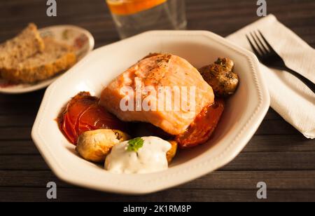 Gedünstetes Meerforellenfilet auf gebratenen Pilzen mit Tomaten in einer weißen Schüssel serviert Stockfoto