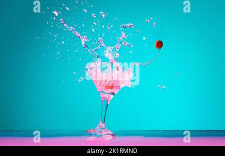 Martini-Cocktail mit Kirschen, die auf blauem Hintergrund in Neonlicht plätschern Stockfoto