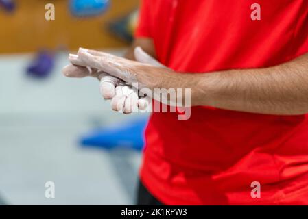 Mann verteilt flüssiges Magnesium auf seine Hände, um Kletterwand zu üben Stockfoto