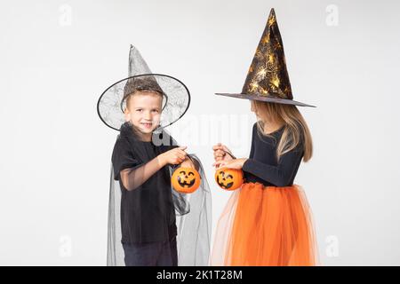 Halloween Für Kinder. Ein schönes Mädchen in einem Hexenkostüm und ein Junge in einem Zauberer-Kostüm nehmen Süßigkeiten aus einem Korb in Form von Jacks Laterne. Kind h Stockfoto