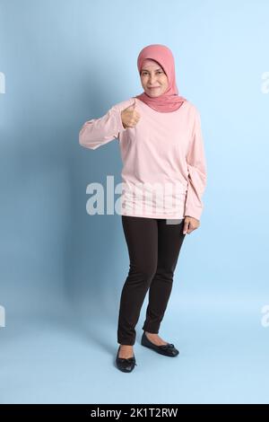 Die ältere südostasiatische Frau mit dem Hijab, der auf dem blauen Hintergrund steht Stockfoto