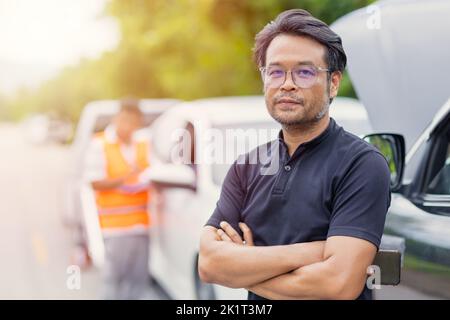 Intelligenter asiatischer erwachsener Mann, der am Straßenrand lächelt, weil er wegen eines Autounfalls zufrieden war. Er löste Probleme und der Service des Versicherten-Teams war gut Stockfoto