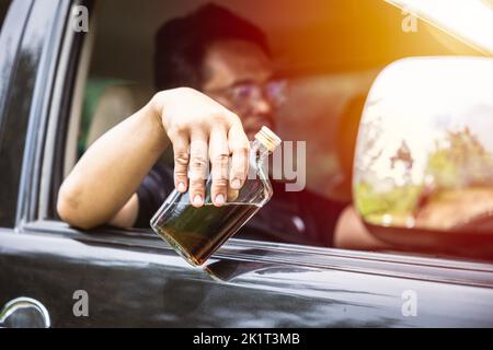 Mann betrunken während der Fahrt ein Auto. Fahrer mit Alkohol Whisky Flasche gefährlich und illegal Konzept. Stockfoto