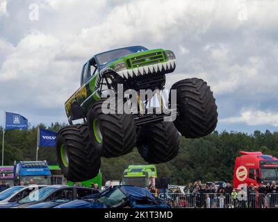 Sumpf-Ding Monster-Truck, der über Autos springt, hat mitten im Sprung actiongeladene Fotos aufgenommen Stockfoto