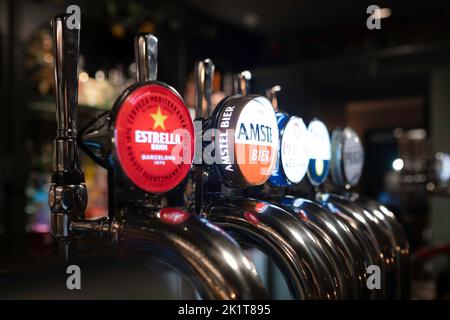 Edelstahl-Bierzapfhähne, Craft Beer in einem englischen Pub, verschiedene Marken. Auf das Schild „Amstel Bier“. Enge Schärfentiefe, Seitenansicht Stockfoto