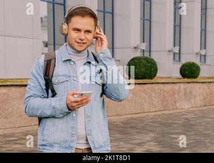 Junger lächelnder Mann mit Kopfhörern und Rucksack im Freien Stockfoto