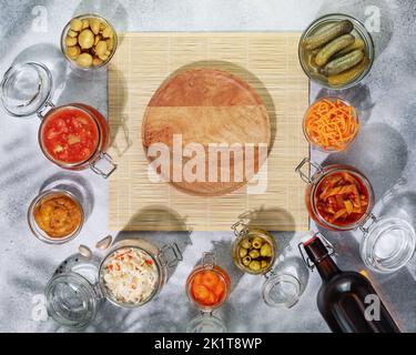 Probiotische Lebensmittel. Eingelegte oder fermentierte Produkte. Fermentiertes Gemüse und Pilze in Gläsern, Flasche mit selbstgemachtem Bier um leeren Holzteller Stockfoto