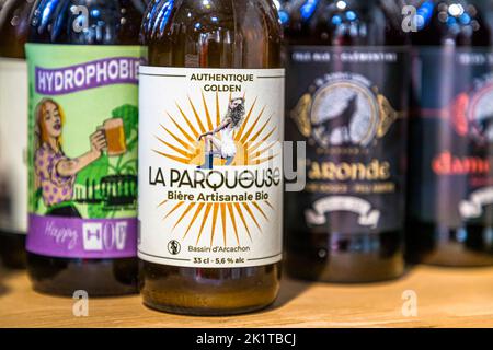 Die Flasche „La Parqueuse“ von der Brauerei Les Brasseurs de l'Océan in Lacanau, Médoc, Frankreich, zeigt eine sitzende Frau vor stilisierten Sonnenstrahlen und trägt den Zusatz „Authentique Golden – Bière Artisanale Bio – Bassin d'Arcachon“. Der Name bezieht sich auf die Parqueusen, die Frauen, die traditionell in den Austernbetten des Bassin d'Arcachon arbeiten. Im Hintergrund stehen weitere Biere der Brauerei, darunter „Hydrophobie“ und „L'Aronde“. Stockfoto