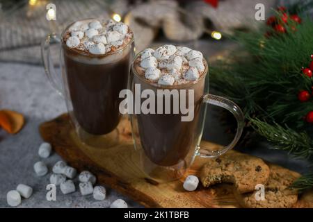 Heiße Schokolade in Glaskrügen mit Mini-Marschmalven auf grauem Tisch, verschwommener Weihnachtshintergrund Stockfoto