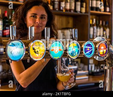 Der Besitzer der Brauerei Les Brasseurs de l'Océan in Lacanau, Médoc, Frankreich, schenkt ein Glas La Canaulaise-Bier aus einem Sechsauslaufspender ein. Die runden Zapfschilder zeigen sechs verschiedene Biere, die von der Brauerei produziert werden. Stockfoto
