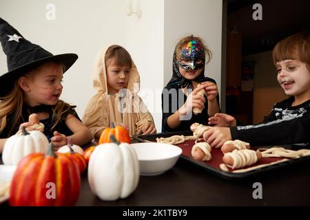 Kinder in Halloween Kostümen kochen gemeinsam am Tisch Stockfoto