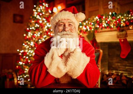 Vorderansicht Porträt des traditionellen Weihnachtsmannes lächelnd auf Kamera ruhend Kopf auf den Armen mit weihnachtsbaum im Hintergrund Stockfoto