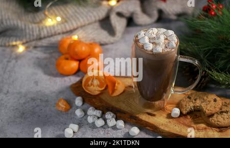 Heiße Schokolade in einem Glaskrug mit Mini-Marschmalven auf Holzplatte, verschwommener Weihnachtshintergrund Stockfoto