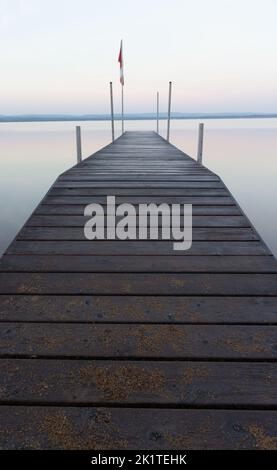 Ein Dock in den frühen Pastelltönen der Morgendämmerung, Sommer magischen Minimalismus auf einem See der perfekten Ruhe. Stockfoto