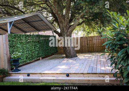 Eine kleine, druckbehandelte Holzterrasse mit einer grünen, überdachten Wand zur Garage Stockfoto