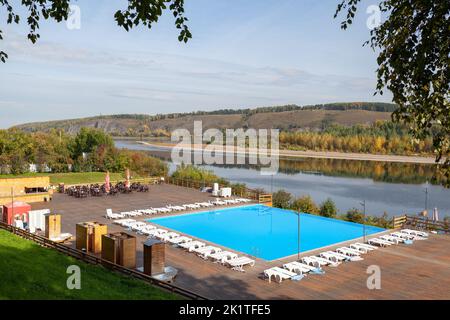 Blauer Pool ohne Menschen am Flussufer im Herbst. Ein großartiger Ort zum Entspannen und Entspannen in der Natur. Der Pool und die Sonnenliegen warten auf Besucher Stockfoto