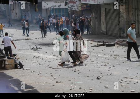 Nablus, Palästina. 20. September 2022. Während der Zusammenstöße in der Stadt Nablus im besetzten Westjordanland laufen Frauen an einer Gruppe von Demonstranten vorbei. Die Palästinenser haben mit den palästinensischen Sicherheitskräften kollapiert, während sie gegen die Verhaftung von zwei Mitgliedern der islamischen Widerstandsbewegung Hamas protestierten. (Foto von Nasser Ishtayeh/SOPA Images/Sipa USA) Quelle: SIPA USA/Alamy Live News Stockfoto