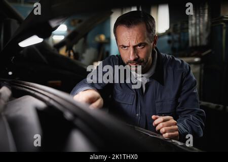 Portrait von reifen Auto Mechaniker Reparatur Motor im Geschäft mit intensiven Gesichtsausdruck Stockfoto