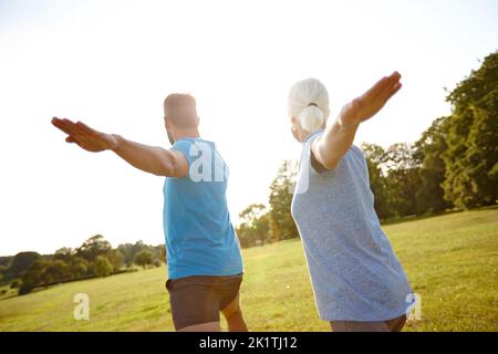 Beenden Sie den Tag mit etwas Yoga. Rückansicht eines reifen Paares, das im Freien Yoga macht. Stockfoto