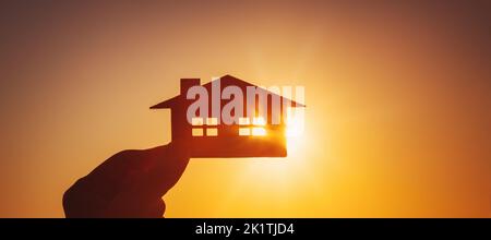 Die Hand einer Frau, die am Abend des Sonnenuntergangs ein Modell eines Hauses hält Stockfoto
