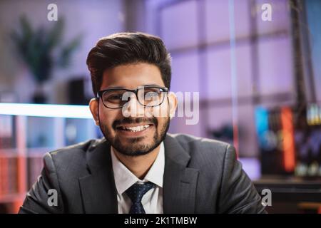 Nahaufnahme eines selbstbewussten indischen Geschäftsmanns oder Wirtschaftswissenschaftlers in formeller Kleidung und Brille, der im Nachtbüro vor der Kamera posiert. Stockfoto