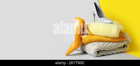Stapel von stylischen Pullovern und Damenschuhen auf farbigem Hintergrund mit Platz für Text Stockfoto