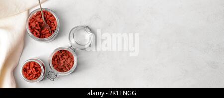 Gläser mit getrockneten Goji-Beeren auf hellem Hintergrund mit Platz für Text Stockfoto